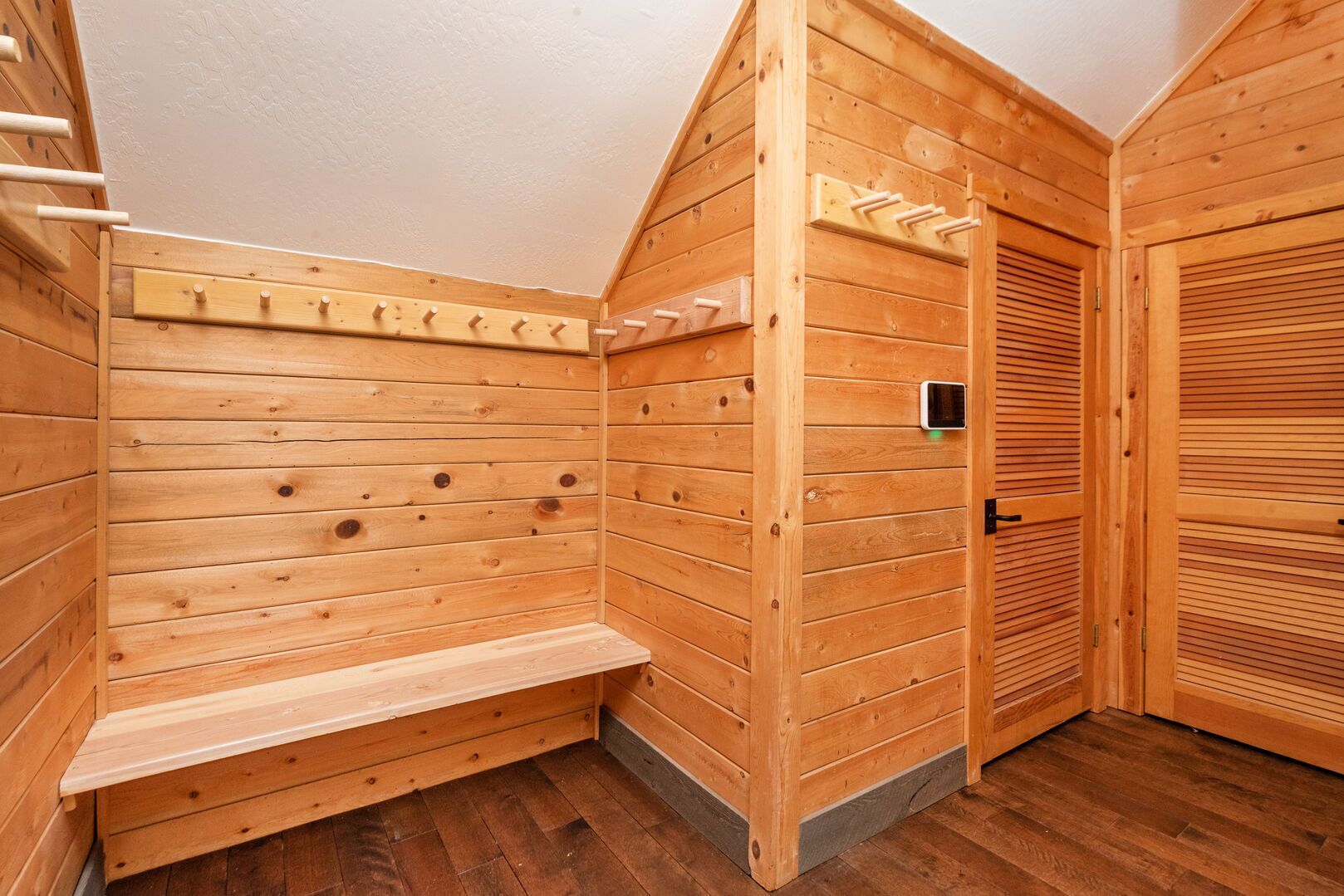 A wooden sauna with a bench, a door with a handle, and a wall-mounted towel rack.