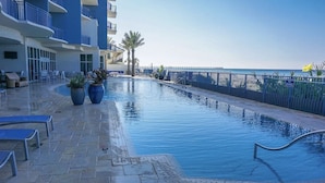 A swimming pool with lounge chairs and potted plants, surrounded by a fence and a building with balconies.