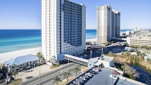 A high-rise hotel with a beach view, multiple parking lots, and a clear sky.