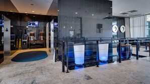 A modern lobby with a reception desk, digital screens, a seating area, and a large window.