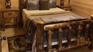 Une chambre à coucher dans un chalet en bois, avec un lit, deux tables de chevet, des lampes, un ventilateur de plafond et une tête de lit en bois.