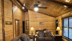 L’intérieur chaleureux d’un chalet en bois comprend deux canapés en cuir, un ventilateur de plafond et une grande fenêtre.