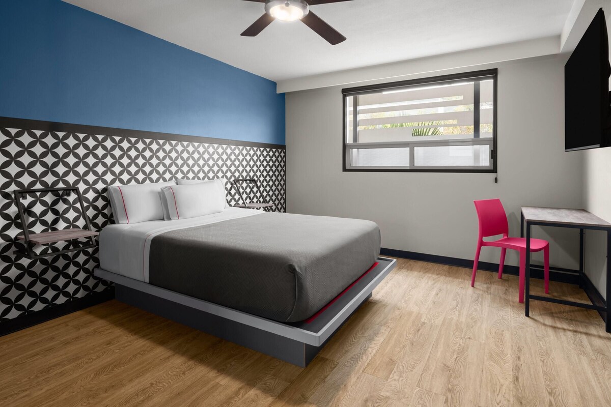 Quarto com cama, escrivaninha, cadeira, ventoinha no teto e janela.