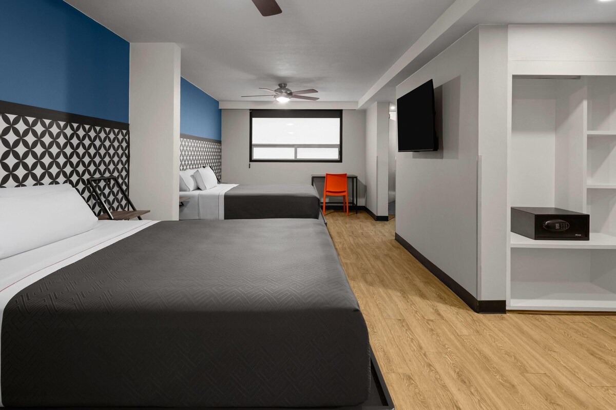 Quarto de hotel com cama grande, escrivaninha, cadeira, televisão e janela.
