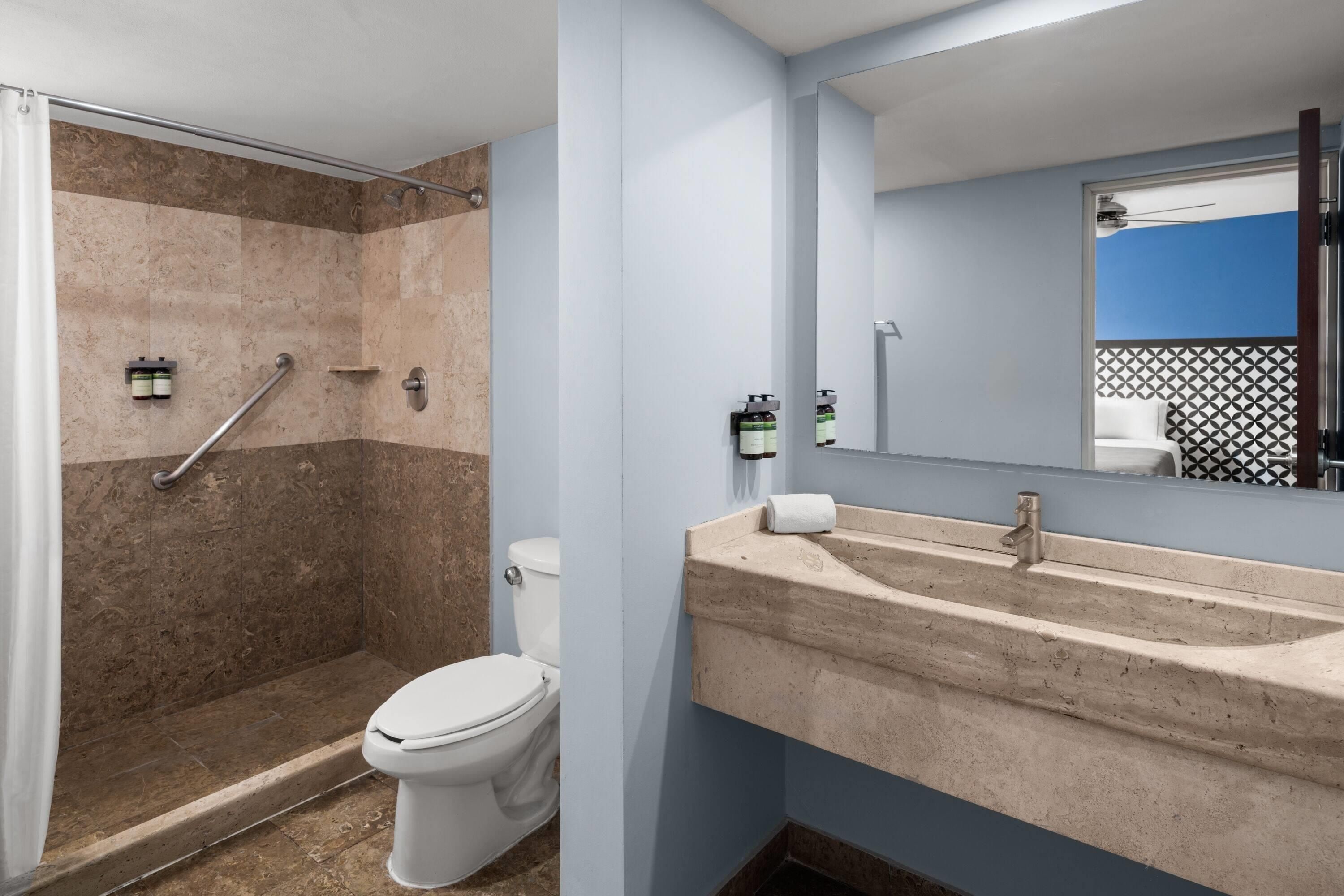 A bathroom with a shower, toilet, sink, and a mirror.
