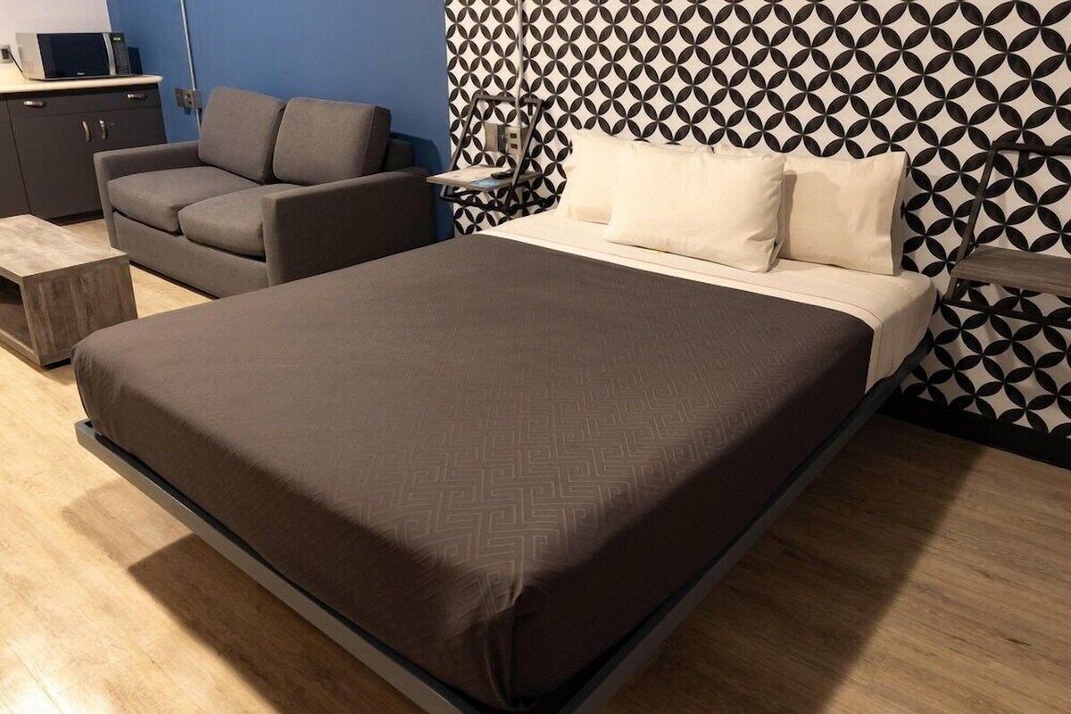 A bedroom with a bed, a sofa, a nightstand, and a microwave on the dresser.