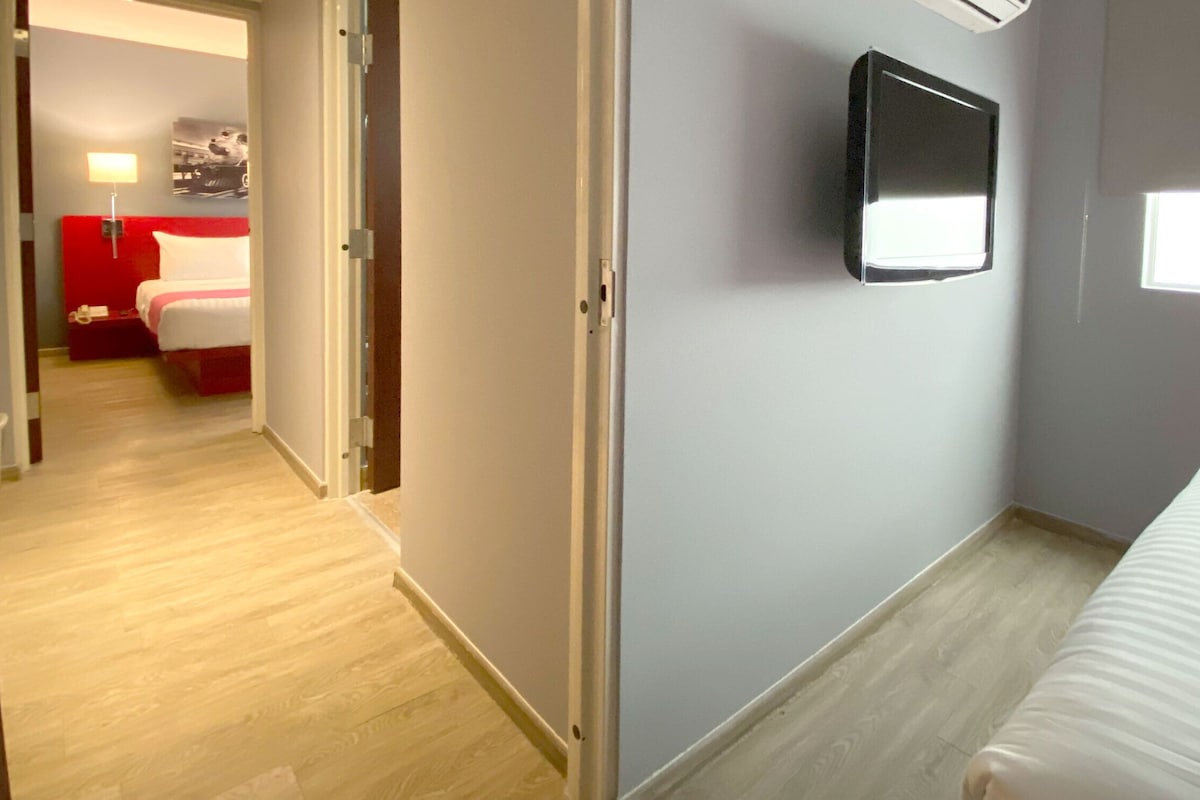 A hotel room with a bed, a TV mounted on the wall, and a window.