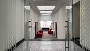 A modern hallway with glass doors, red seating, and a skylight. - Hotel MX forum buenavista CDMX, Trademark by Wyndham (Mexico City)