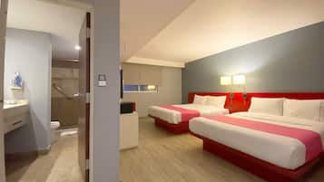 Two beds with red headboards and white bedding, a desk with a chair and lamp, and a bathroom in this stylish room.