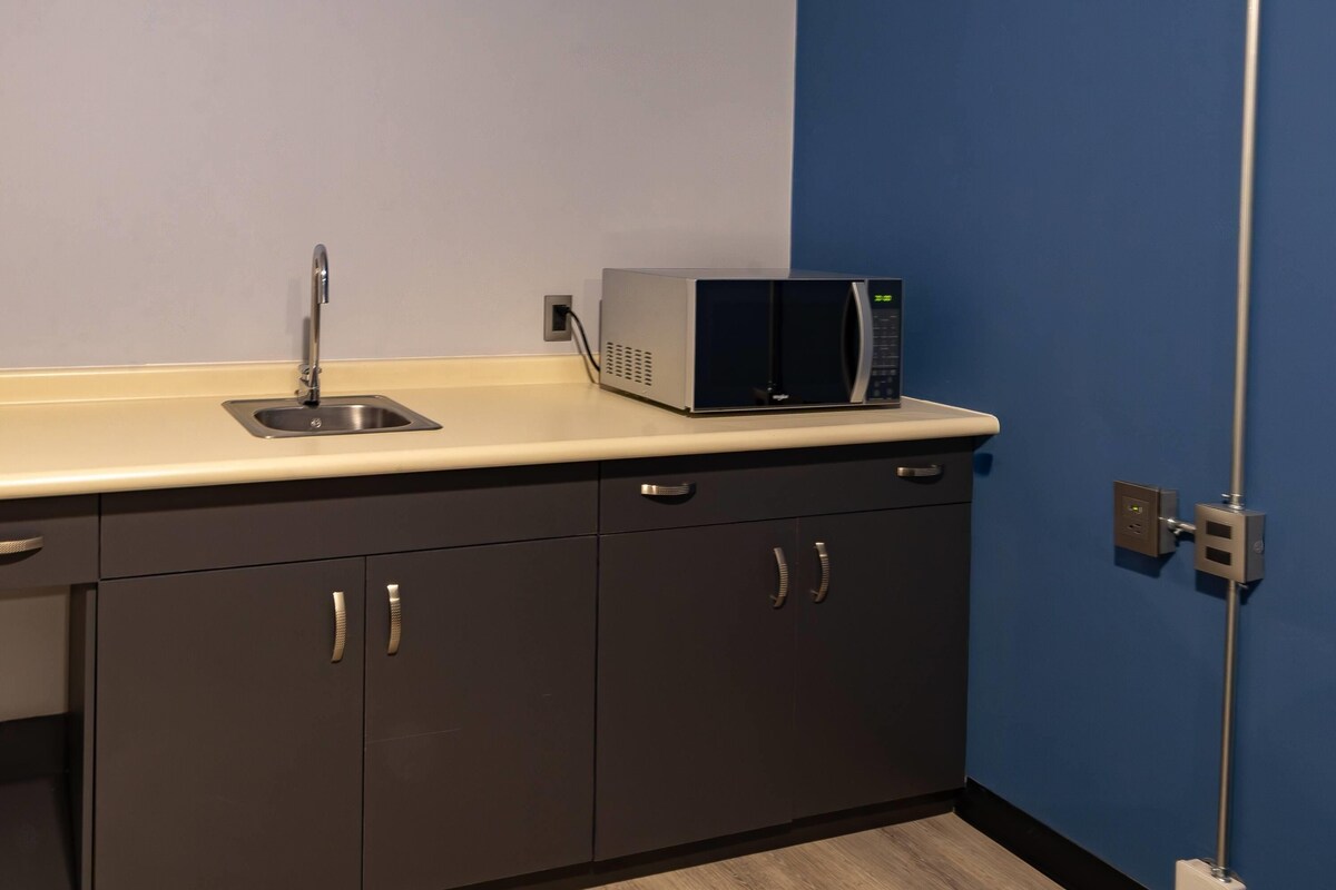 A kitchenette with a microwave, sink, and cabinets.