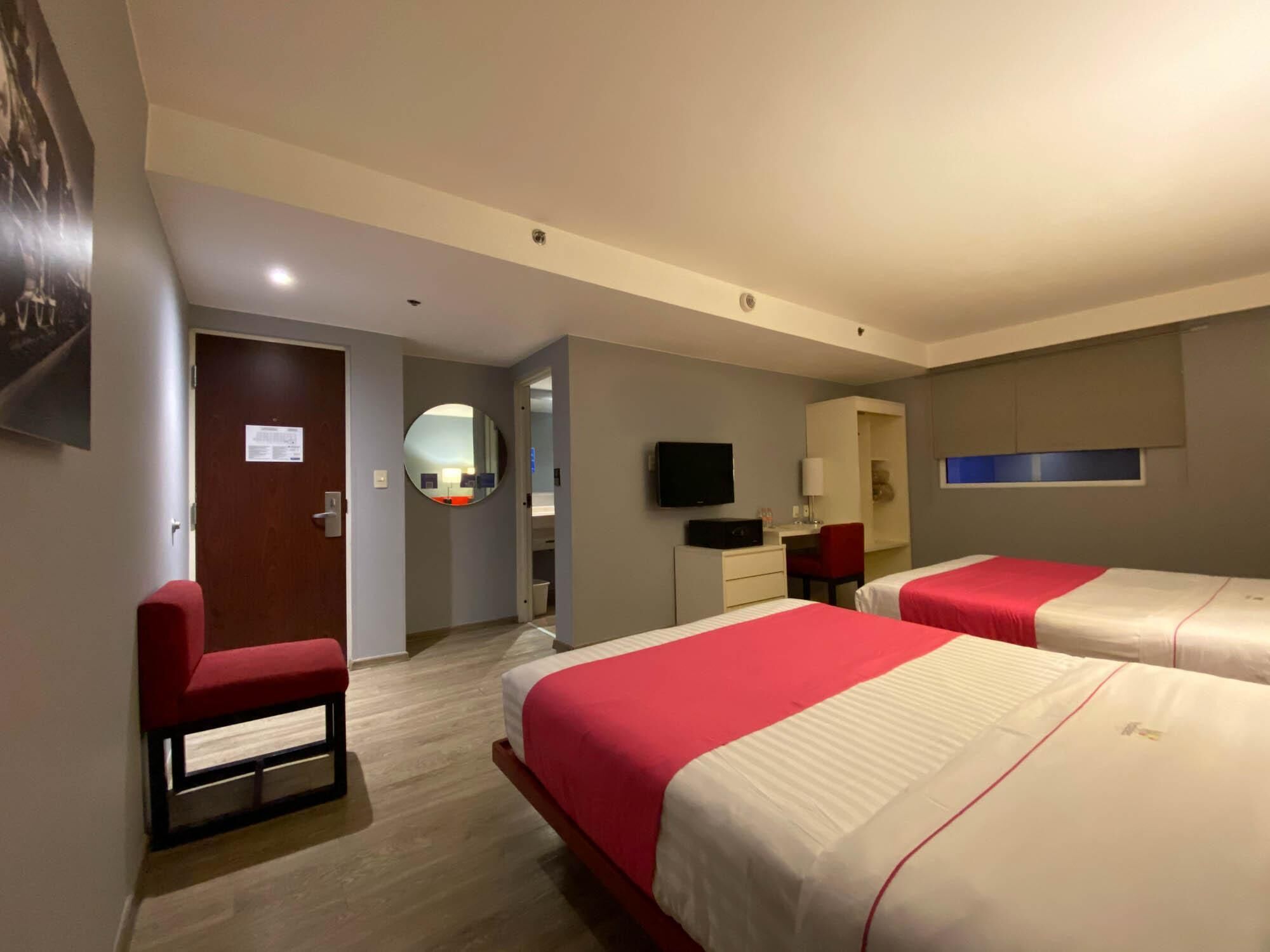 A hotel room with two beds, a desk, a chair, a TV, and a mirror.