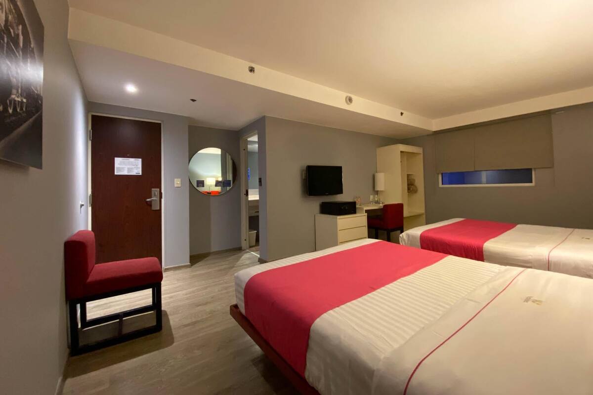 Ein Hotelzimmer mit zwei Betten, einem Schreibtisch, einem Stuhl, einem Fernseher und einem Spiegel.