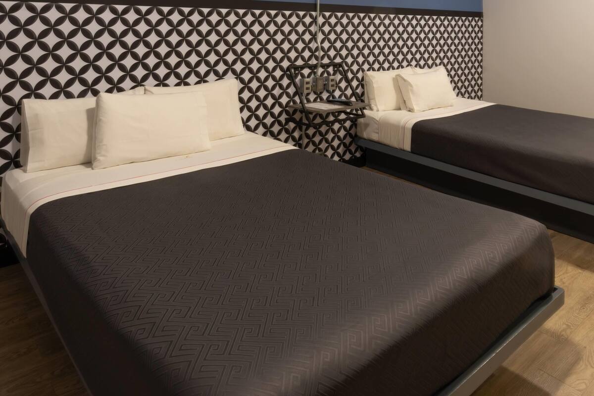Ein Hotelzimmer mit zwei Betten, einem gemusterten Kopfteil und einem Nachttisch.