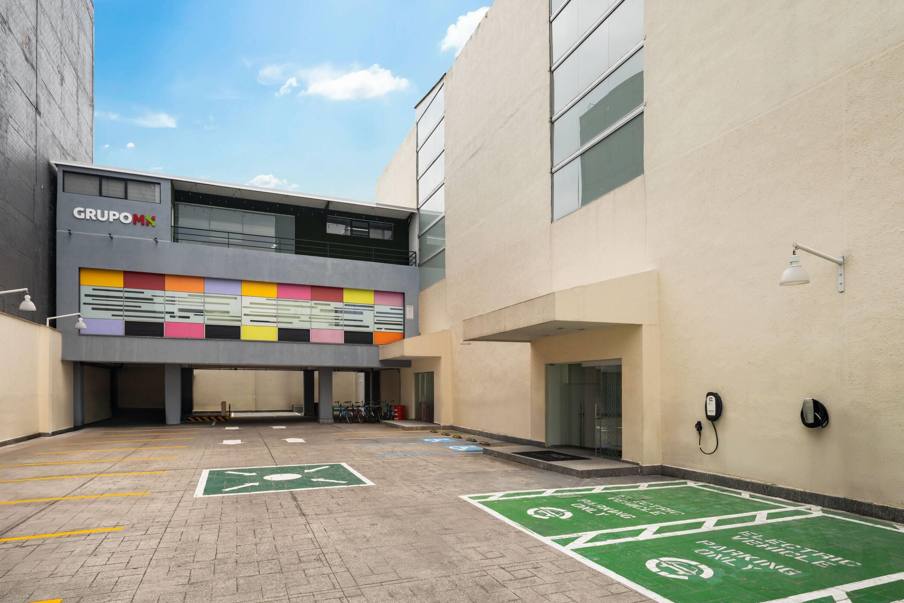 Un bâtiment moderne doté d’une façade colorée et d’un espace de stationnement équipé de bornes de recharge pour véhicules électriques.