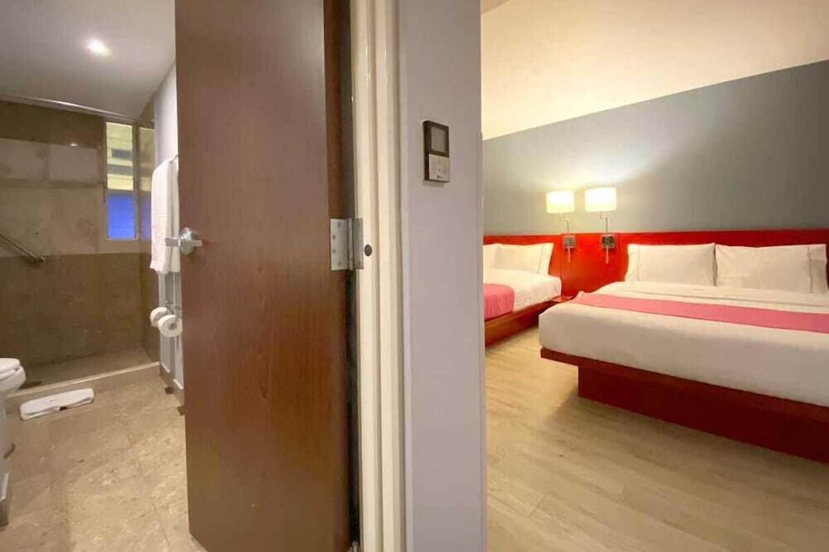 A hotel room with a shower, a bed with red headboard, and a bedside table.