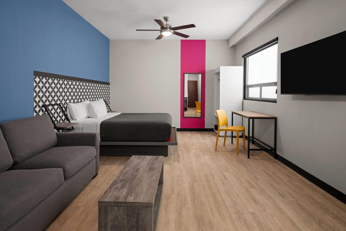 Quarto de hotel moderno com cama, sofá, escrivaninha e televisão.