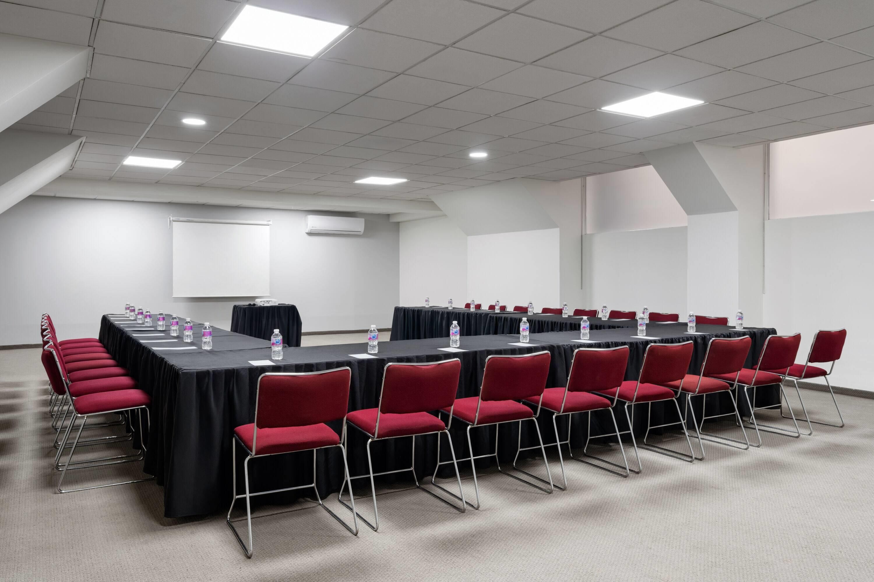 A conference room with a long table, red chairs, and water bottles.
