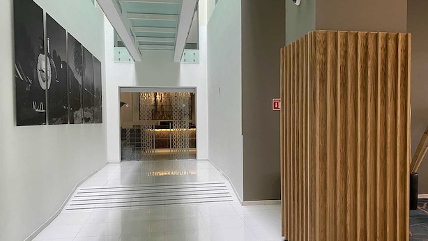 A modern hallway with a wooden partition, tiled flooring, and a glass door leading to a room with a patterned interior. - Hotel MX forum buenavista CDMX, Trademark by Wyndham (Mexico City)
