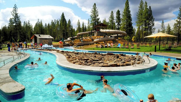 A swimming pool with multiple lanes, a water slide, and a small building in the background. - Pet friendly, hot tub, ping pong (Sunriver)