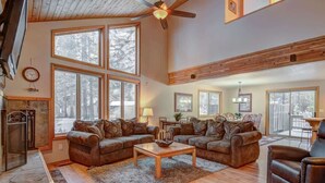 A spacious living room with a fireplace, large windows, and a ceiling fan. - Pet friendly, hot tub, ping pong (Sunriver)