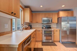 A modern kitchen with wooden cabinets, stainless steel appliances, and a large window providing natural light. - Pet friendly, hot tub, ping pong (Sunriver)