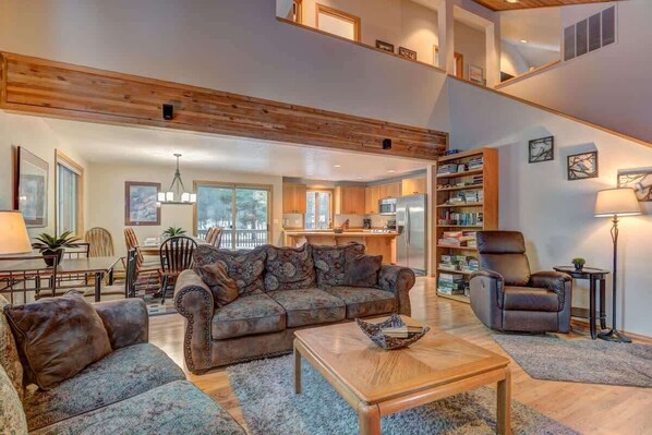 A spacious living area with a high ceiling, a sofa set, a coffee table, and a bookshelf.