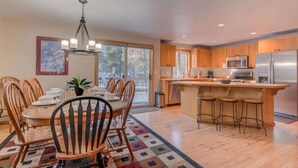 A modern kitchen with wooden cabinets, a central island with bar stools, a dining area with a round table and chairs, and a chandelier. - Pet friendly, hot tub, ping pong (Sunriver)