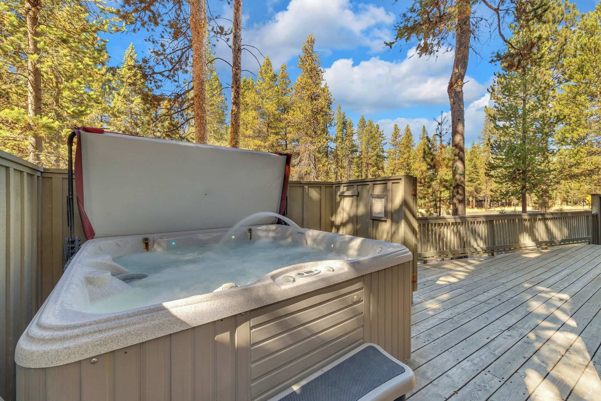 A hot tub on a wooden deck with a wooden fence and trees in the background.