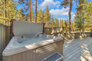 A hot tub on a wooden deck with a wooden fence and trees in the background.