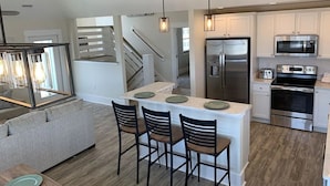 Una cocina moderna con una isla central, electrodomésticos de acero inoxidable y una escalera que sube a otro nivel.