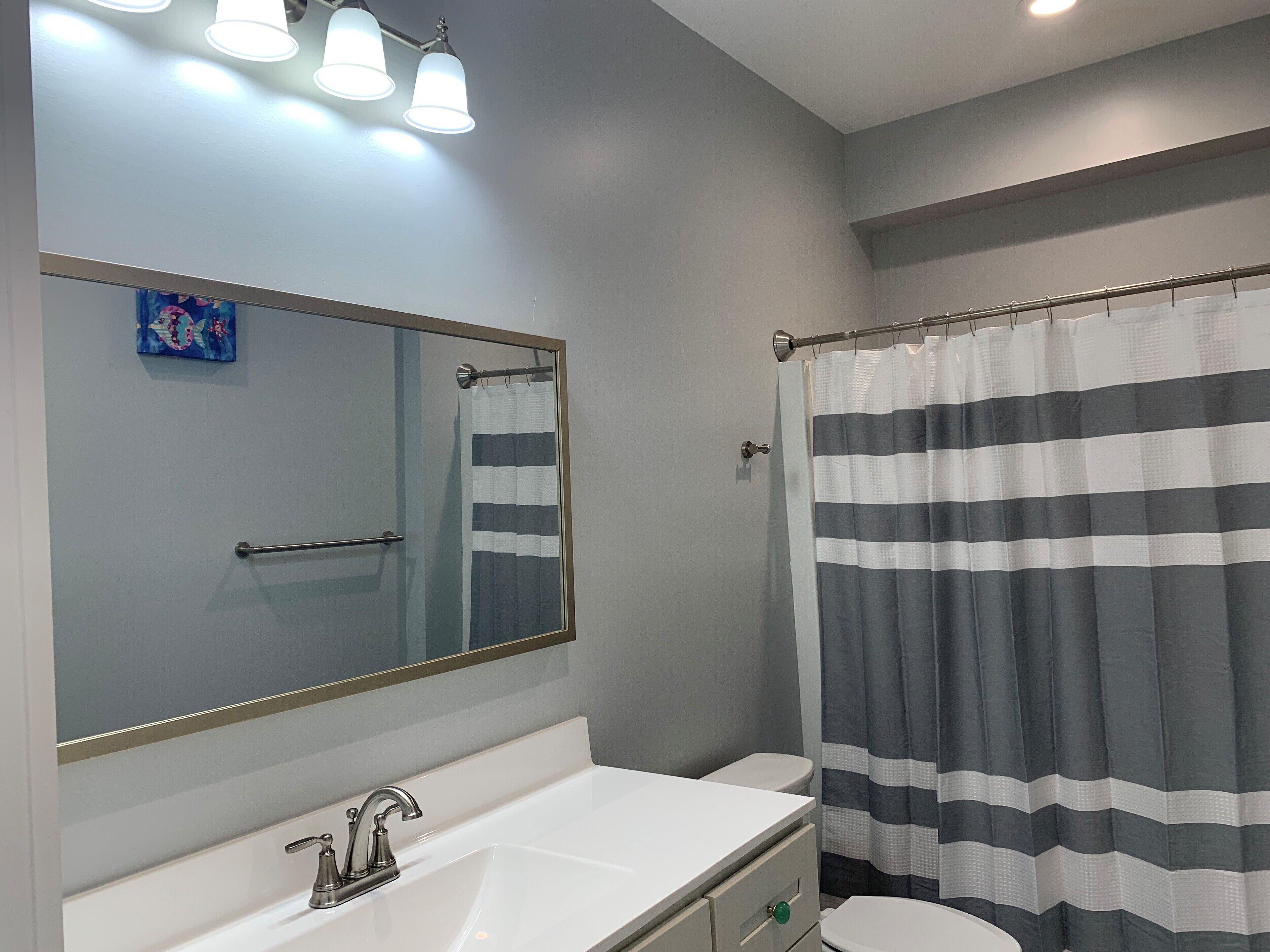 A bathroom with a white sink, a mirror, a toilet, and a striped shower curtain.