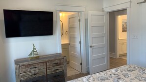 Un dormitorio con cama, cómoda, televisor y puerta que da a un baño.