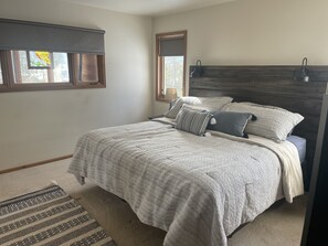 A bedroom with a bed, a headboard, a window with blinds, a mirror, and a rug.