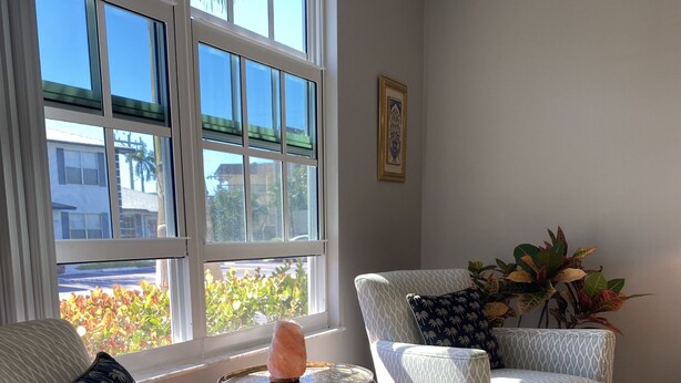 A living room with two patterned armchairs, a small side table with a salt lamp, and a view of the outside through large windows. - Sun Filled Townhome w/Pool, 5' to beach, walk to bars/restos, luxury bath/shower (Marco Island)