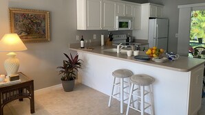 A modern kitchen with white cabinets, a central island with stools, a microwave, and a refrigerator. - Sun Filled Townhome w/Pool, 5' to beach, walk to bars/restos, luxury bath/shower (Marco Island)