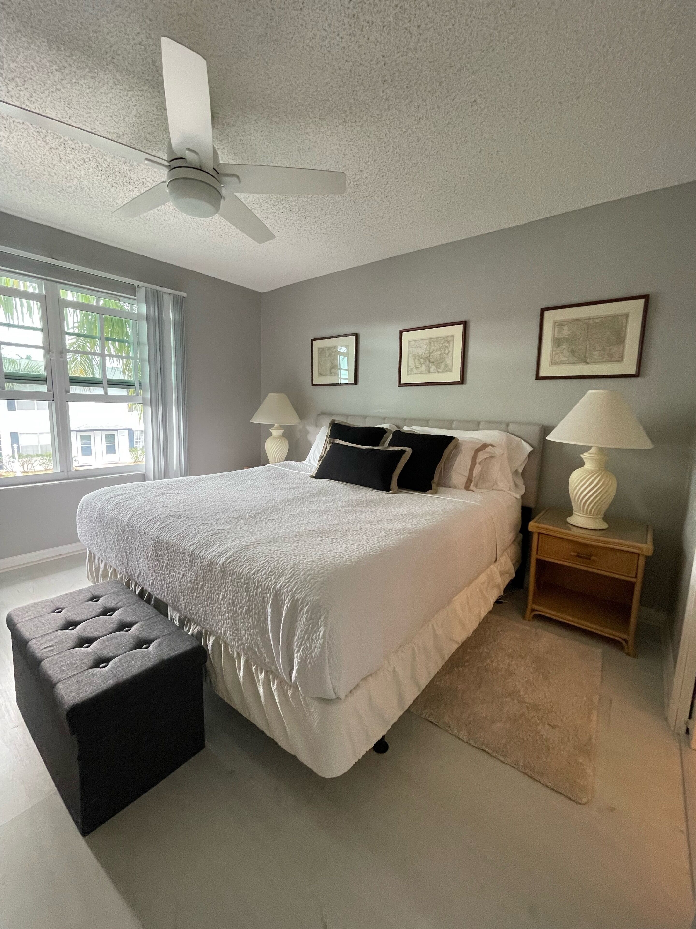 A bedroom with a bed, a ceiling fan, a window, and framed pictures on the wall.