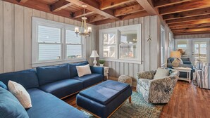 Un salon spacieux avec un canapé d’angle bleu, un fauteuil à motifs et un plafond en bois.