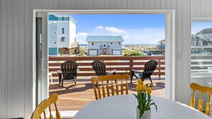 Une terrasse avec une table et des chaises, une plateforme en bois et une vue sur une maison de plage.