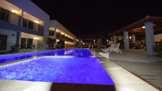 Ein Swimmingpool mit blauer Beleuchtung, angrenzende Liegestühle und ein Gebäude mit mehreren Balkonen und Außenbereichen zum Sitzen.