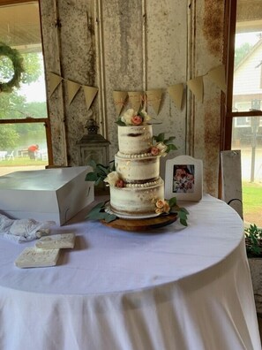 A wedding cake on a table with a white tablecloth, surrounded by greenery and a framed photo. - Events&Pets 👍 * Weddings* Retreats*Nature*Hot Tub w/ central location! (Cumming)