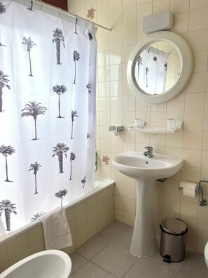 Een badkamer met een bad, wastafel, toilet, spiegel en een prullenbak.