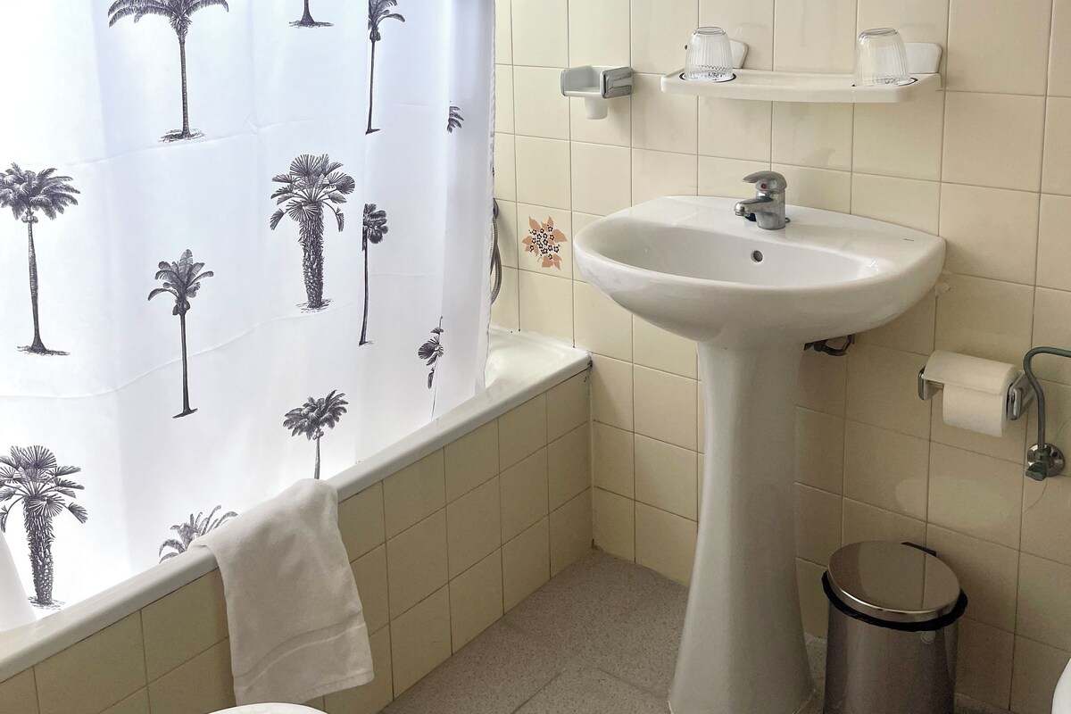 Un baño con bañera, lavamanos, inodoro, espejo y cubo de basura.