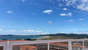 A coastal view from a balcony with a clear sky, a beach, and distant hills. - Bluesea Costa Norte (Sanxenxo)