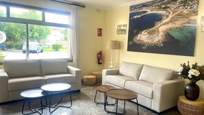 A modern living room with a beige sofa, two round tables, and a large painting of a coastal landscape. - Bluesea Costa Norte (Sanxenxo)