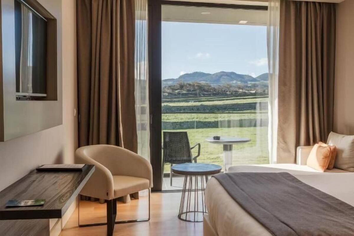 Ein Hotelzimmer mit Bett, Schreibtisch, Stuhl, einem kleinen Tisch und Blick auf eine Landschaft.