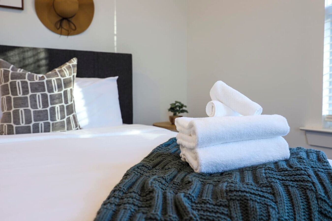 A neatly made bed with a dark green knitted blanket, white pillows, and folded white towels on the side.