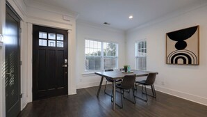 Une pièce avec un plancher en bois foncé, une porte noire, une table à manger avec quatre chaises et un tableau accroché au mur.