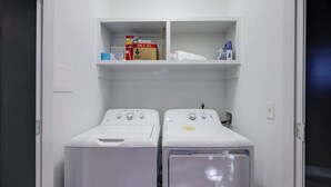 Une buanderie équipée de deux machines à laver à chargement frontal et d’étagères au-dessus, où sont rangés les produits de nettoyage.