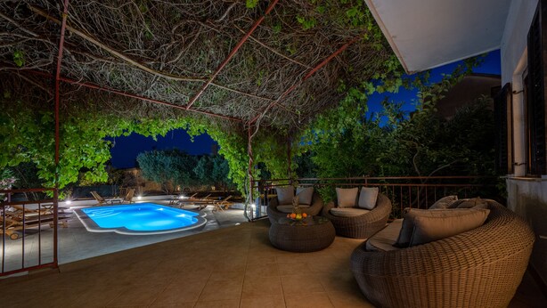Un espace extérieur avec une piscine, des meubles en osier et une vue sur les arbres la nuit.