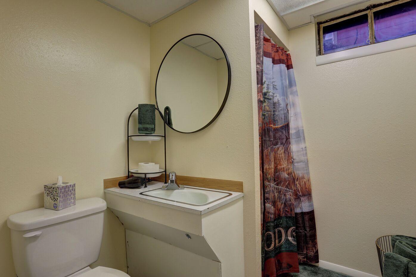 A small bathroom with a toilet, sink, and mirror. There is a towel rack with a towel hanging on it.